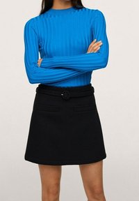 Blau gerippter Langarmoberteil mit Rundhalsausschnitt, kombiniert mit einem schwarzen Rock, der einen Gürtel und zwei vordere Taschen hat.