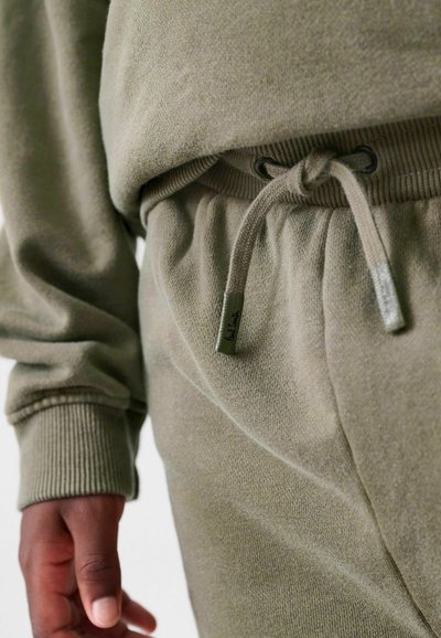 Olivengrøn joggersæt med en blød tekstur, elastisk talje med snor og ribbede manchetter. Diskret logo-detail på taljen.