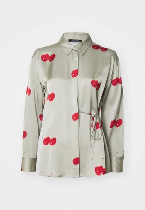 Zelena satenska srajca z ovratnikom na gumb, dolgimi rokavi in rdečimi češnjevimi potiski. Ima zavezo pri pasu in gladko teksturo.