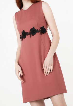 Sleeveless dusty rose dress with black floral lace band across the waist, worn by a person with fair skin and long red hair.