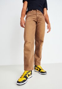 Bruna jeans i denim med rak ben design, som har en klassisk femficksstil och en subtil textur, i kombination med svarta och gula sneakers.