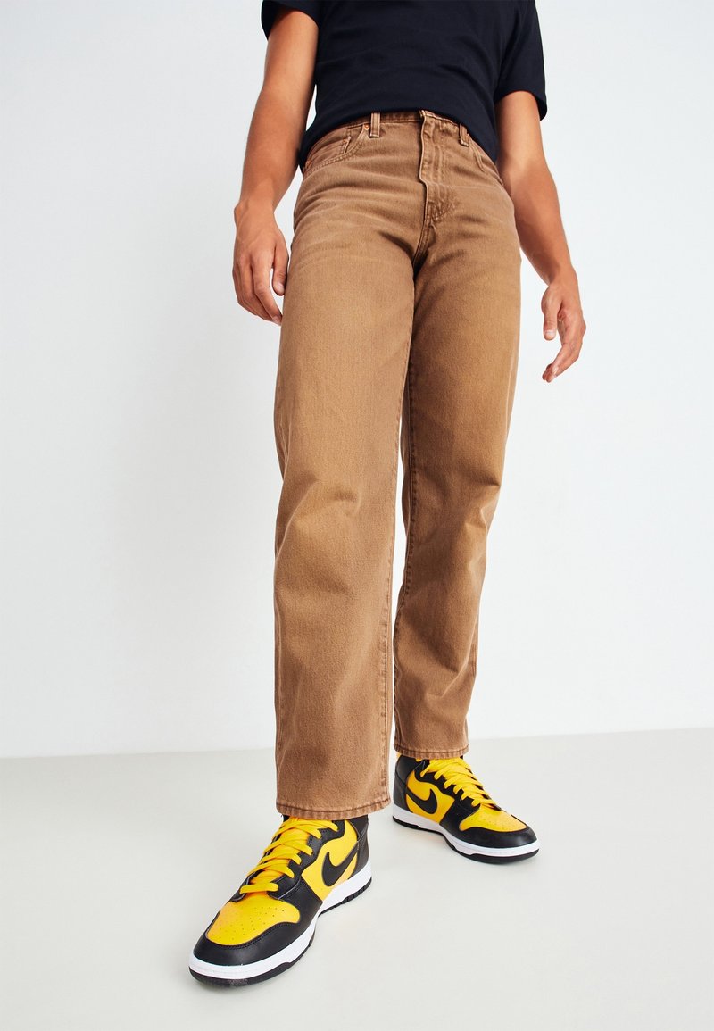 Bruna jeans i denim med rak ben design, som har en klassisk femficksstil och en subtil textur, i kombination med svarta och gula sneakers.