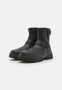 Botas de cuero negro hasta el tobillo con punta redondeada, detalle de hebilla lateral y suela de goma texturizada y rugosa. Presentan un eje de altura media.
