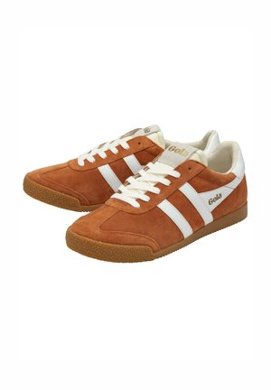 Sneakers in suede marrone con strisce e lacci bianchi. La suola in gomma presenta un motivo testurizzato. Il marchio è visibile sul lato e sulla linguetta.