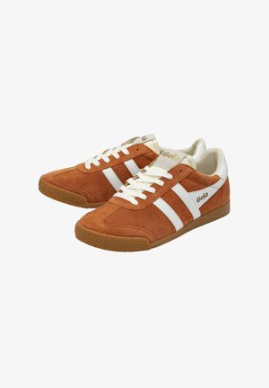 Zapatillas de ante marrón con rayas y cordones blancos. La suela de goma presenta un patrón texturizado. La marca es visible en el costado y en la lengüeta.