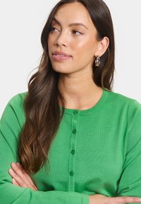 Cardigan verde realizzato in tessuto a maglia con scollatura a girocollo, dotato di sei bottoni coordinati sul davanti e un design aderente.