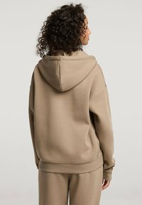 Przestronna beżowa hoodie z kapturem na sznurki, ribbanym mankietem i miękką fakturą. Tył jest prosty, bez dodatkowych ozdób.