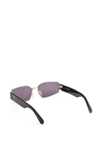 Gafas de sol con lentes morados angulares, marco delgado de metal dorado y brazos de plástico negro. Almohadillas nasales texturizadas para mayor comodidad, acentos de logo en las patillas.