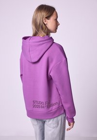 Felpa viola con una vestibilità rilassata, caratterizzata da un grande cappuccio, fessure laterali e una stampa di testo grafica sul retro in basso.