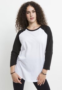 Vit raglan t-shirt med svarta ärmar, med rund halsringning och mjuk, slät bomullstyg. Avslappnad passform med rundad nederkan.