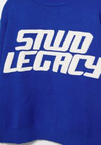 Blauwe gebreide trui met een gedurfde witte "STUD LEGACY" opdruk op de voorkant. Geribbelde manchetten en zoom met een ronde hals.