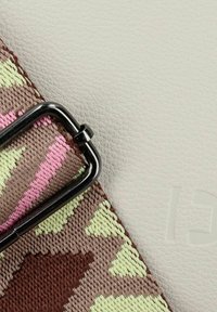 Cinghia in tessuto texturizzato di colore marrone con motivi verdi e rosa, fissata con una fibbia in metallo nera, su uno sfondo in pelle grigia chiara e liscia.