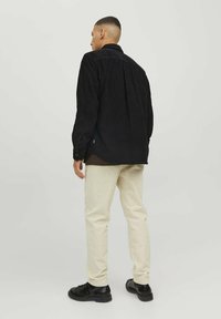 Zwarte corduroy-overhemd met lange mouwen, gecombineerd met beige broek en zwarte schoenen. Het overhemd heeft een button-down kraag en zijkleppen.