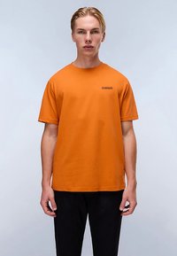 Orangefärgad t-shirt i bomull med rund halsringning och korta ärmar, med en liten svart logotyp på vänster bröst.