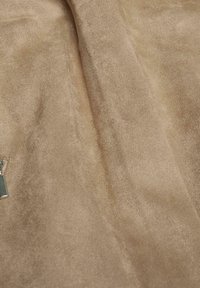 Beige suede stof met een zachte, gladde textuur. Voorzien van een ritssluiting met een klein metalen label eraan bevestigd. Subtiele glans over het oppervlak.