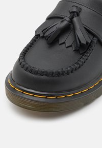 Zwarte leren moccasin schoen met een gestructureerd oppervlak, decoratieve kwastjes, verfijnde stiksels en een contrasterende gele zool.