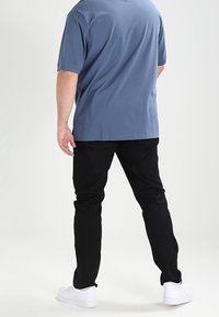 Blå kortärmad skjorta, svarta byxor och vita sneakers. Skjortan har en avslappnad passform och byxorna är slim-fit, med en mjuk textur.