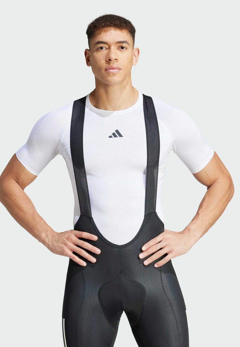 Schwarze Radsport-Bib-Shorts mit Netzträgern, kombiniert mit einem eng anliegenden weißen feuchtigkeitsableitenden Shirt mit schwarzem Logo auf der Brust.