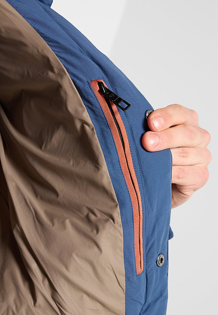 Interno di una giacca blu e beige con una tasca con zip che presenta un accento arancione. Il materiale sembra leggero e liscio.