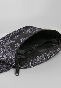 Borsa in tessuto nero con motivo paisley bianco, apertura con zip e interno liscio. Presenta materiale testurizzato e forma curva.