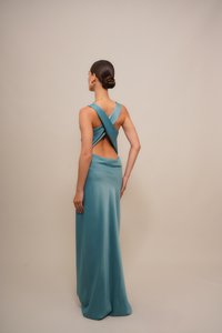 Une robe longue en satin teal avec un dos croisé, une texture lisse et une silhouette ajustée qui épouse élégamment le corps.