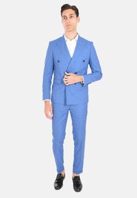 Abito blu chiaro doppiopetto con pantaloni slim fit, tessuto texturizzato e mocassini neri. Camicia bianca visibile sotto il blazer.