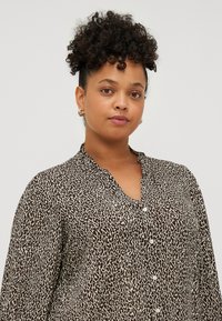 Blouse à imprimé animal marron et crème avec col, fermeture à boutons et manches longues. Confectionnée dans un tissu doux et texturé.