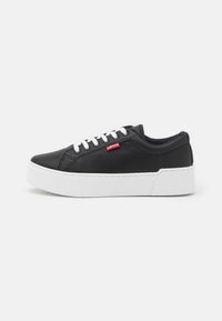 Mustad sünteetilised spordijalatsid mustas värvis, valge kummitald, valged kingapaelad ja väike punane Levi'si logo küljel. Madala lõikega disain.
