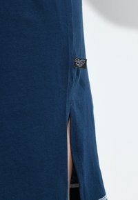 Granatowa koszulka z miękkiej bawełny, z bocznym rozcięciem i małą czarną metką na dolnym brzegu. Prosty design, krótkie rękawy.