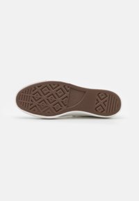 White sneaker sole features a brown rubber outsole with textured diamond and horizontal patterns. The upper edge is smooth with minimal detailing.