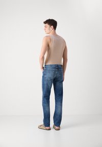 Top fără mâneci bej cu dungi, blugi denim într-o nuanță de albastru deschis, croială lejeră, finisaj texturat, purtat cu sandale bej, văzut din spate.