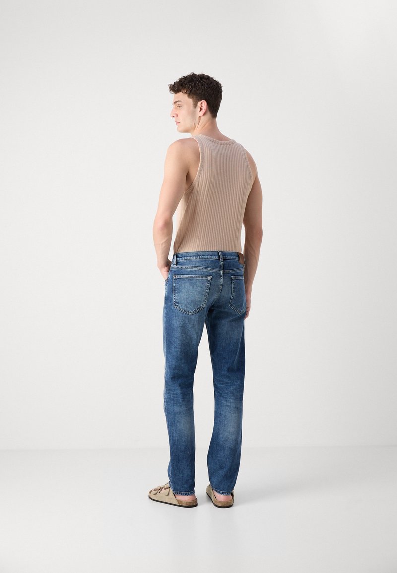 Beige gerippter Tanktop, helle Jeans in entspannter Passform mit strukturiertem Finish, getragen mit tanfarbenen Sandalen, von hinten sichtbar.