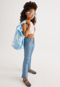 Vaaleansininen tye-dye-takki, hopeinen crop-top, siniset leveälahkeiset farkut ja mustat kengät, joissa on valkoisia pilkkuja. Lisävarusteina aurinkolasit ja choker-kaulaketju.
