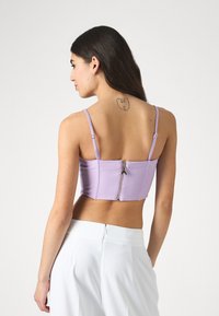 Lavender crop top with adjustable straps, structured design, and a silver zipper at the back. Smooth fabric and fitted shape.