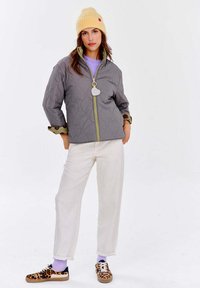 Šedá prešívaná bunda so žltým zipsom, vzorovými manžetami, skombinovaná s bielymi nohavicami a teniskami s leopardím vzorom, doplnená žltou čiapočkou.