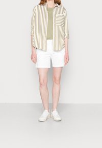 Chemise à manches courtes rayée beige et blanche, assortie à un short blanc et des baskets blanches. Design simple, look décontracté.