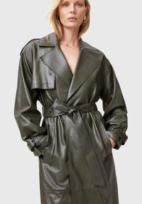 Trench coat in pelle verde oliva con ampio colletto, vita con cintura e grandi tasche, caratterizzato da una superficie liscia e una vestibilità rilassata.