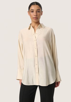 Long-sleeve, light beige shirt made of soft fabric with a button-down front, rounded hem, and relaxed fit. Features cuffed sleeves.