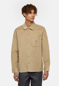 Beige corduroy overhemd met een button-down kraag, voorzak en logodetail; heeft lange mouwen en een gestructureerde stof.
