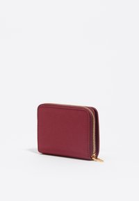 Billetera burdeos hecha de material texturizado, con cierre de cremallera dorada, forma rectangular y diseño minimalista.