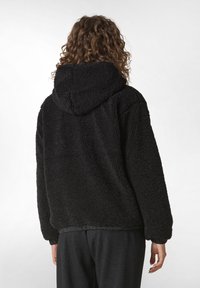 Felpa nera in pile, morbida e pelosa, con cappuccio regolabile, polsini e orlo a costine. Tessuto soffice, vestibilità oversize, senza motivi o dettagli visibili.