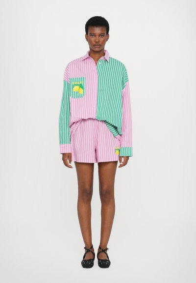 Stribet skjorte i lyserøde og grønne nuancer med en citron grafisk lomme. Sammen med matchende lyserøde shorts. Sorte flade sko med krydsede stropper.