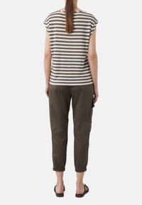 Pasek bluzka z krótkim rękawem w odcieniach beżu i brązu, zestawiona z ciemnozielonymi spodniami ¾. Materiał wydaje się miękki, z luźnym krojem i mankietowymi wykończeniami.