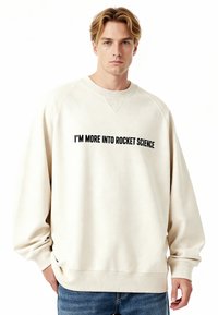 Crèmekleurige sweatshirt met geribbelde manchetten en zoom, met zwarte tekst "I'M MORE INTO ROCKET SCIENCE" over de borst.