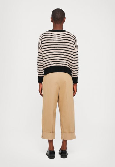 Stripet strikkegenser i svart og krem, med avslappet passform og ribbestrikket nederkant, parret med beige cropped bukser og svarte sko.