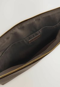 Avoin ruskea laukku, jossa on sileä sisus, varustettu vetoketjullisella sulkimella ja pieni logotagi sisällä.