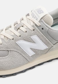 Grijze suède sneaker met gaasaccenten, witte logo, crèmekleurige veters en een gewelfde rubberen zool met kleine studs. Klassiek sportief ontwerp.