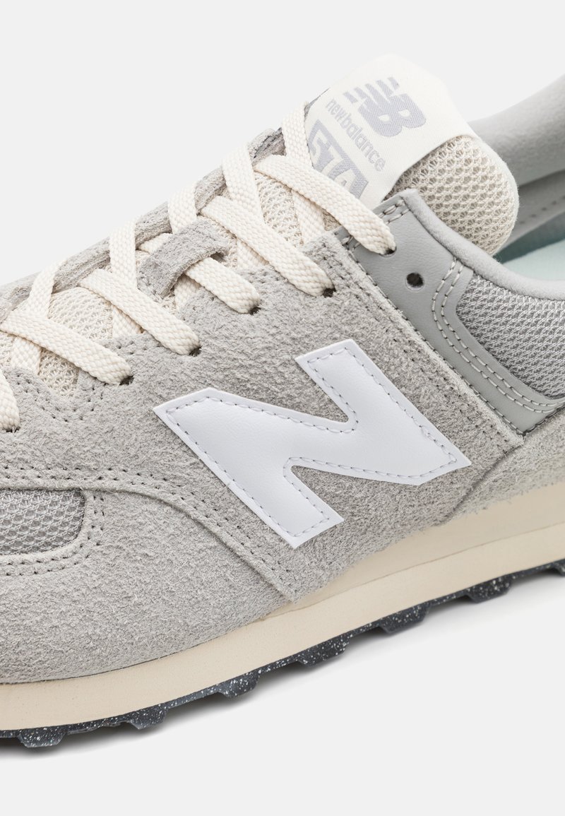 Graue Wildledersneaker mit Mesh-Akzenten, weißen Logo, cremefarbenen Schnürsenkeln und einer strukturierten Gummisohle mit kleinen Nieten. Klassisches sportliches Design.