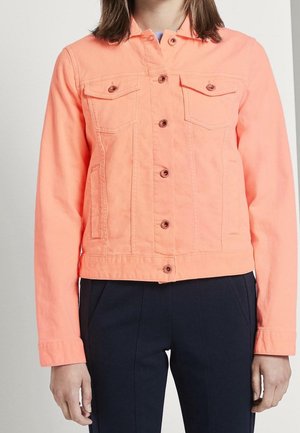 Personne portant une veste boutonnée corail vif avec poches poitrine et manches longues, associée à un pantalon foncé.