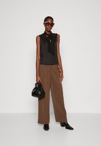 Blusa nera senza maniche con dettaglio a fiocco, pantaloni larghi marroni, borsa nera e stivali neri con tacco spesso. Elegante, texture liscia.
